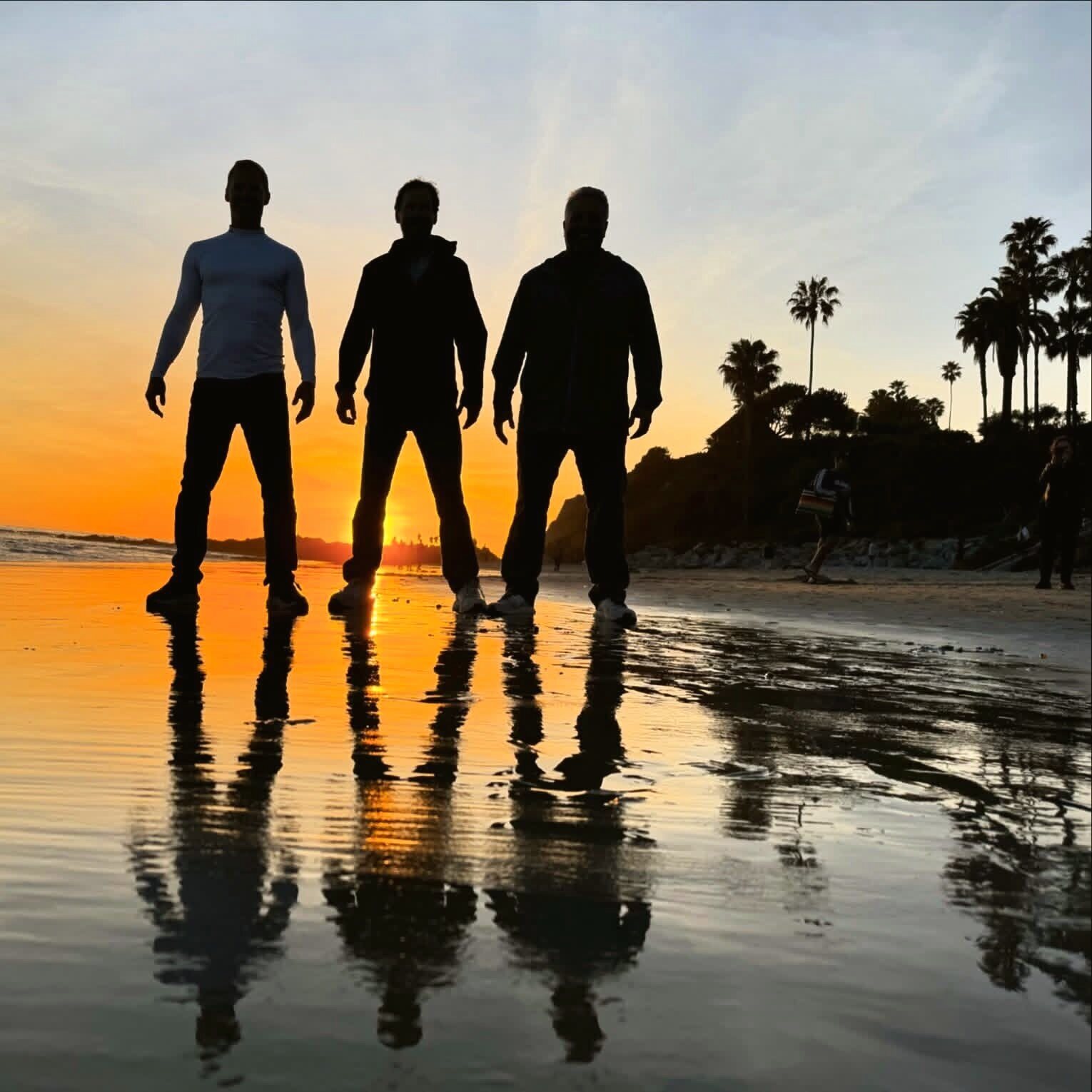 Three men at golden hour on a mirror-flat beach